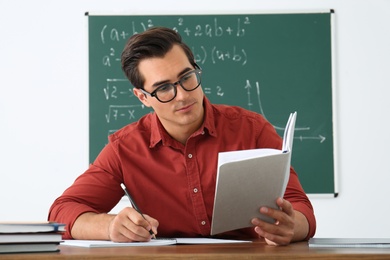 Photo of Young teacher working at table in classroom