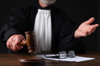 Photo of Judge with gavel and papers sitting at wooden table against black background, closeup