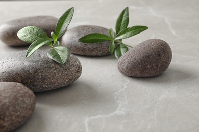 Photo of Spa stones and green leaves on grey table, space for text