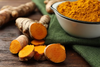 Photo of Bowl with aromatic turmeric powder and cut roots on wooden table, closeup