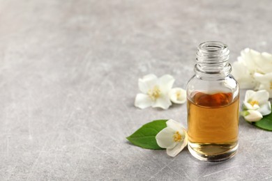 Photo of Essential oil and jasmine flowers on light grey table. Space for text