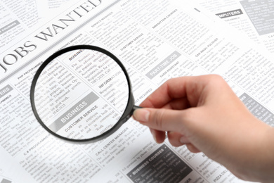 Photo of Woman looking through magnifying glass at newspaper, closeup. Job search concept