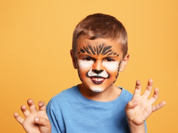 Photo of Cute little boy with face painting on orange background