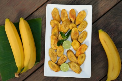 Photo of Tasty deep fried banana slices and fresh fruits on wooden table, flat lay