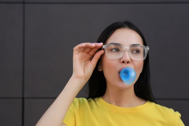 Photo of Beautiful woman blowing gum near dark tiled wall outdoors