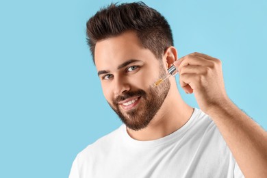 Photo of Handsome man applying cosmetic serum onto face on light blue background