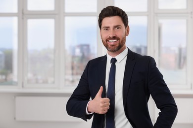 Photo of Happy real estate agent showing thumb up in new apartment. Space for text