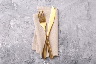 Photo of Elegant golden cutlery and kitchen towel on grey textured table, top view