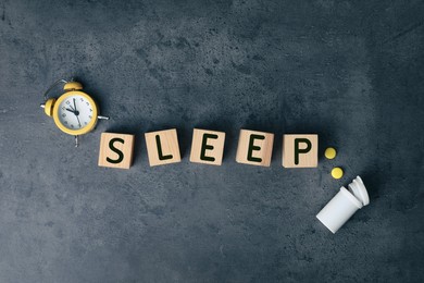 Photo of Word Sleep made of wooden cubes near pills and alarm clock on grey background, flat lay. Insomnia concept