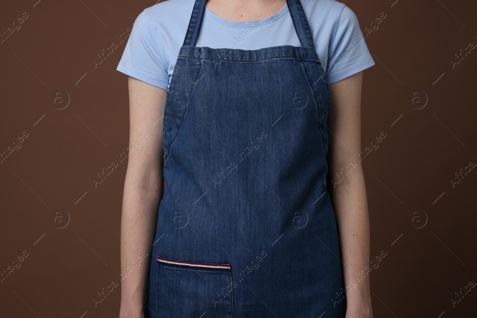 Photo of Woman wearing kitchen apron on brown background, closeup. Mockup for design