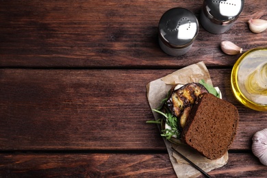 Photo of Delicious eggplant sandwich served on wooden table, flat lay. Space for text