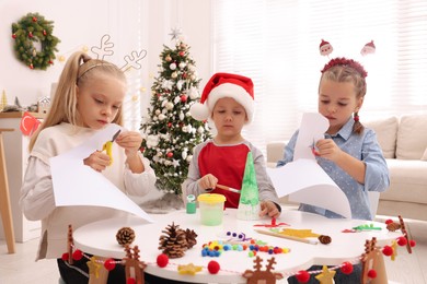 Photo of Cute little children making Christmas crafts at table in decorated room