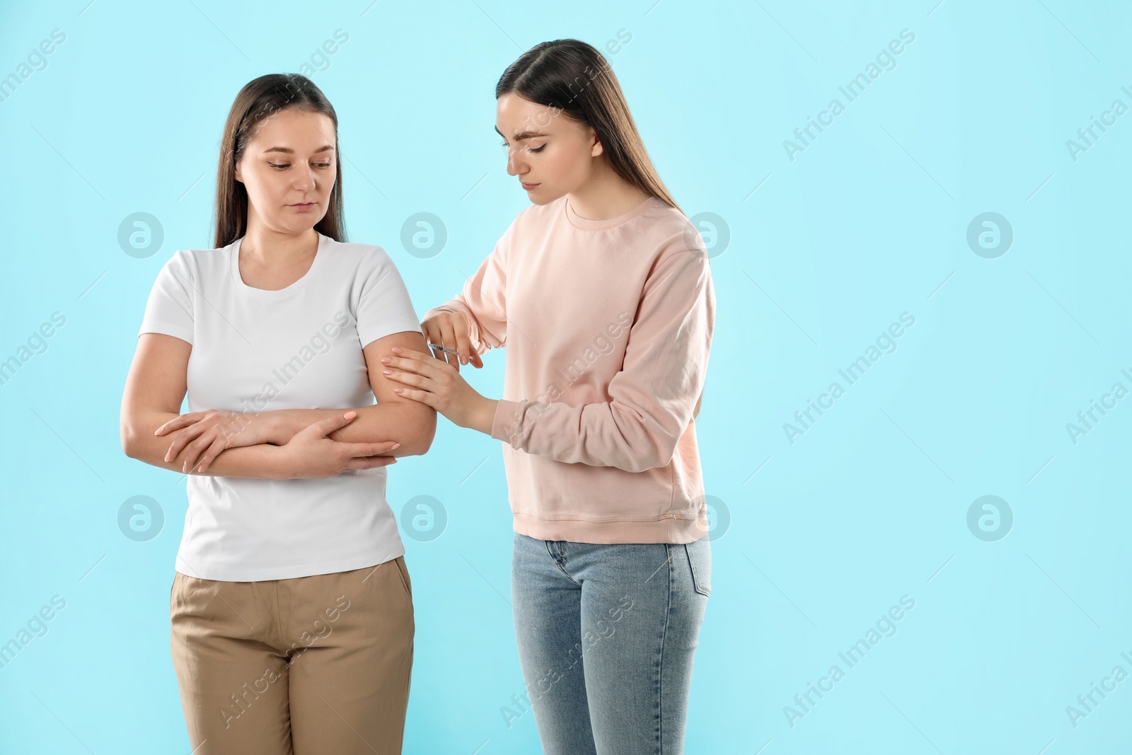 Photo of Woman giving insulin injection to her diabetic friend on light blue background