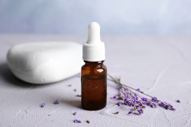 Photo of Natural herbal oil and lavender flowers on table against blurred background