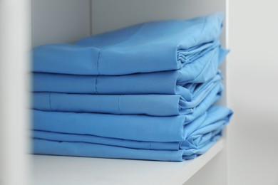 Photo of Light blue medical uniforms on white rack, closeup