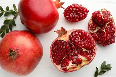 Photo of Pieces of fresh pomegranate and branches on white wooden table, flat lay