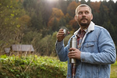 Photo of Man with metallic thermos and cup lid in nature, space for text