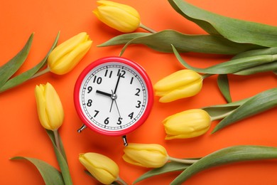Photo of Red alarm clock and beautiful tulips on orange background, flat lay. Spring time