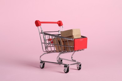 Photo of Small metal shopping cart with cardboard boxes on pink background