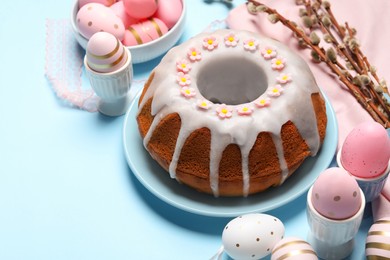 Photo of Delicious Easter cake decorated with sprinkles near painted eggs and willow branches on light blue background