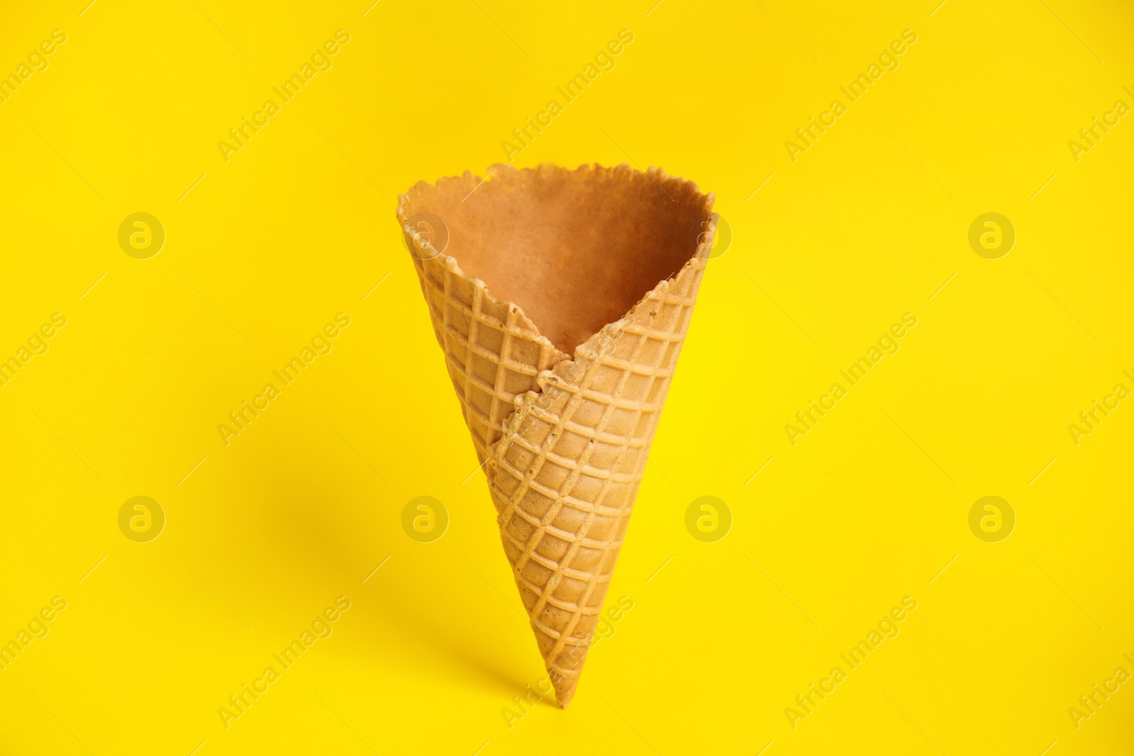 Photo of Empty wafer ice cream cone on yellow background