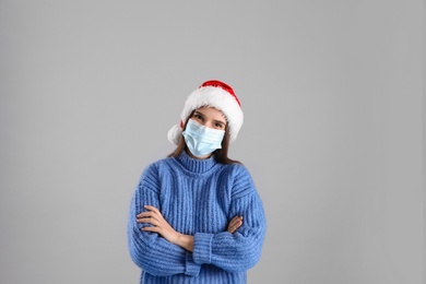 Photo of Pretty woman in Santa hat and medical mask on grey background