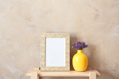 Blank frame and vase with flowers on table near color wall. Mock up for design