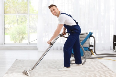 Photo of Male worker removing dirt from carpet with professional vacuum cleaner indoors