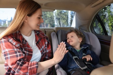 Photo of Cute little boy sitting in child safety seat near mother inside car