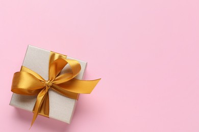 Photo of Gift box with golden bow on pink background, top view. Space for text