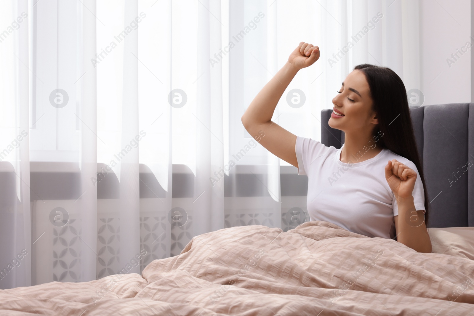 Photo of Beautiful woman stretching on bed at home, space for text. Lazy morning