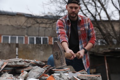 Photo of Man breaking bricks with sledgehammer outdoors, selective focus. Space for text