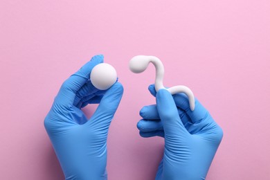 Reproductive medicine. Fertility specialist in gloves holding figures of sperm and egg cells on pink background, top view