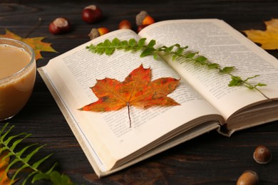 Photo of Book with leaves as bookmark on wooden table, closeup