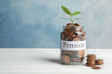 Photo of Glass jar with label PENSION, coins and green plant on white table. Space for text