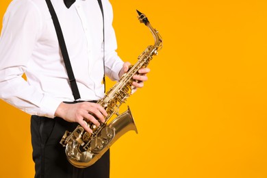 Photo of Man in elegant outfit with saxophone on yellow background, closeup. Space for text