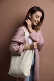 Photo of Happy young woman with blank eco friendly bag against light brown background