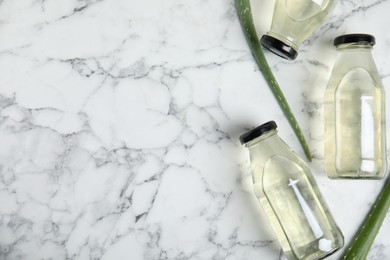 Photo of Fresh aloe drink in bottles and leaves on white marble table, flat lay. Space for text