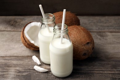 Photo of Bottles of delicious vegan milk and coconuts on wooden table