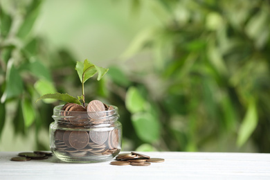 Coins and green sprout on white wooden table against blurred background, space for text. Money savings