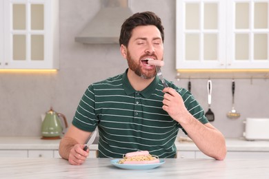 Photo of Man eating sausage and pasta at table in kitchen