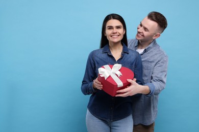 Photo of Boyfriend presenting gift to his girlfriend on light blue background. Space for text