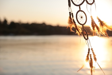 Photo of Beautiful handmade dream catcher near river on sunny day. Space for text
