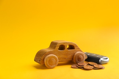 Photo of Wooden car model, key and coins on color background. Space for text