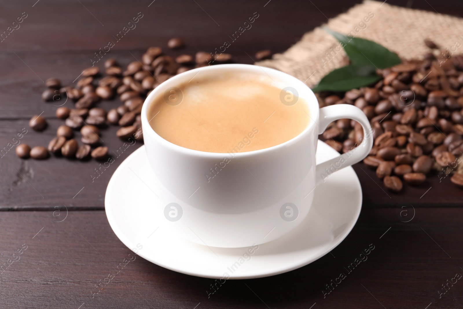Photo of Cup of hot aromatic coffee and roasted beans on wooden table