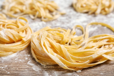 Photo of Uncooked noodles and flour on wooden table, closeup