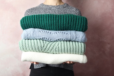 Photo of Woman holding stack of warm clothes on light background, closeup. Autumn season