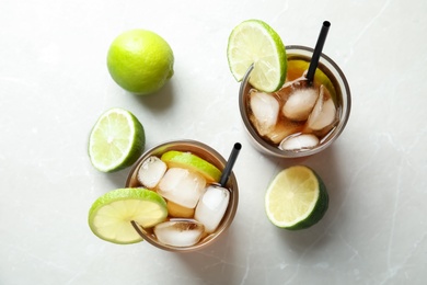 Photo of Glasses of cocktail with cola, ice and cut lime on light background, flat lay