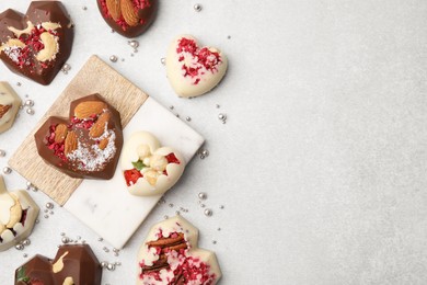 Photo of Tasty chocolate heart shaped candies with nuts on white table, flat lay. Space for text