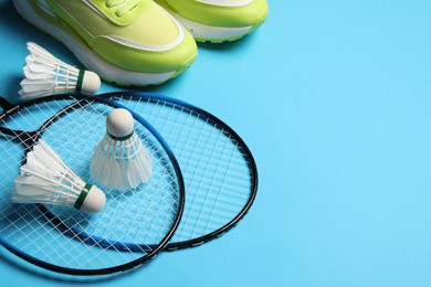 Photo of Feather badminton shuttlecocks, rackets and sneakers on light blue background, space for text